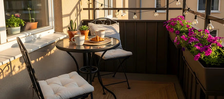 Kleiner Balkon mit Bistrotisch, Metallstühlen, Kaffee und Blumen in Abendsonne