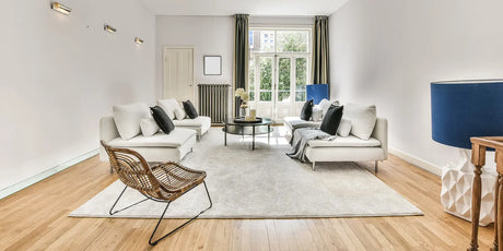 Helles Wohnzimmer mit zwei weißen Sofas, rundem schwarzem Couchtisch und Rattansessel auf grauem Teppich