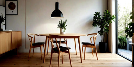 Runder Esstisch aus hellem Holz mit vier Holzstühlen und schwarzen Sitzflächen in skandinavisch eingerichtetem kleinen Esszimmer
