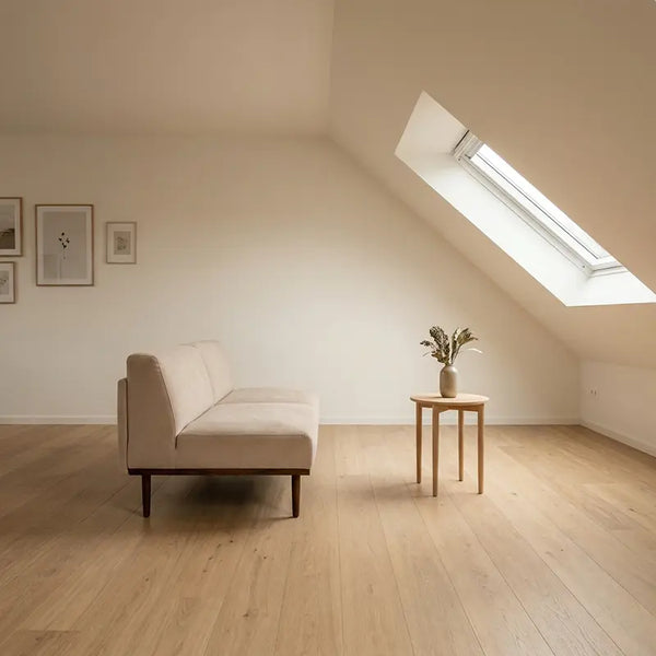 Minimalistisch möbliertes Dachschräge-Zimmer mit niedrigem Sofa, kleinem Beistelltisch und viel offener Fläche