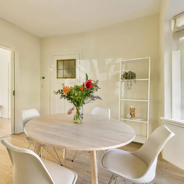 Ovaler Esstisch aus hellem Holz mit weißen Schalenstühlen und Blumenstrauß in freundlichem, hell eingerichtetem Esszimmer