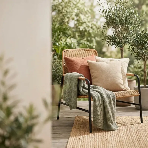 Rattansessel mit Kissen und gestrickter Decke auf Terrasse zwischen Olivenbäumen