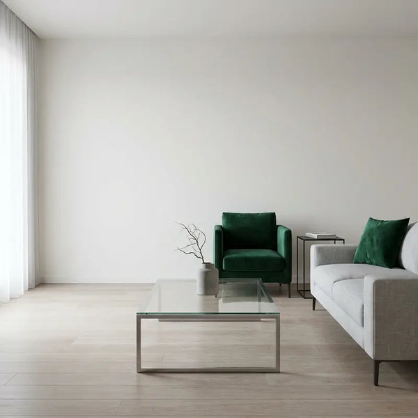 Modernes Wohnzimmer mit Glas-Couchtisch, grauem Sofa und smaragdgrünem Samtsessel als Farbakzent
